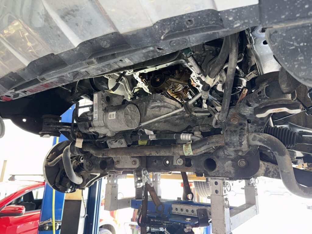 Underside of a Jeep Grand Cherokee during oil pump repair with the lower engine area opened for access.